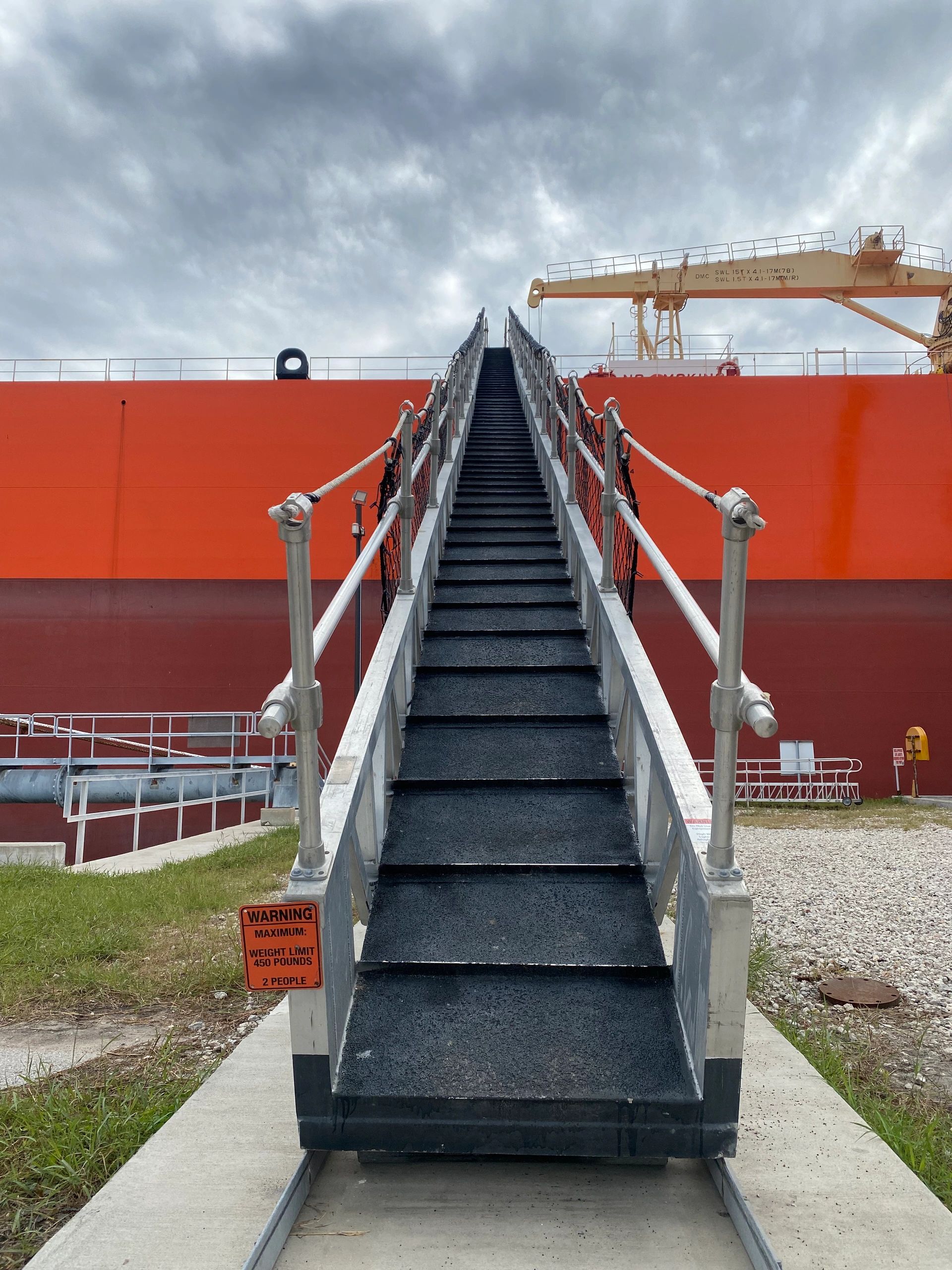 Metal gangway stairs leading up to a large orange ship hull at a bulk liquid marine terminal