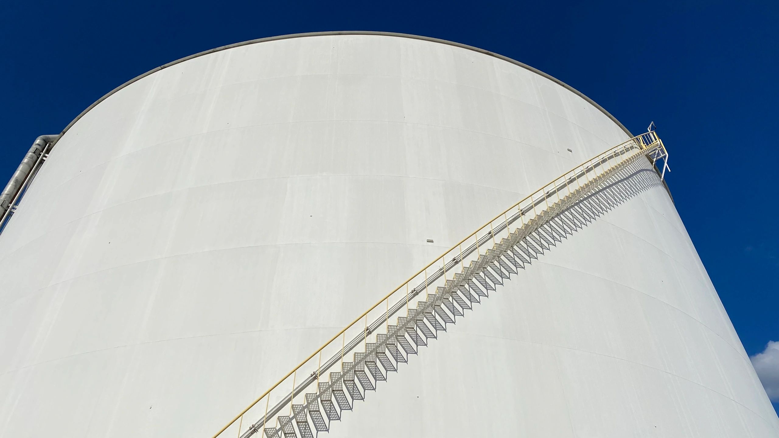 White bulk liquid storage tank with spiral staircase against a clear sky